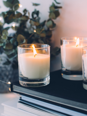 "Elegant home decor close-up featuring eucalyptus sprigs and three white candles arranged on sleek black coffee table books for a modern, minimalist aesthetic.